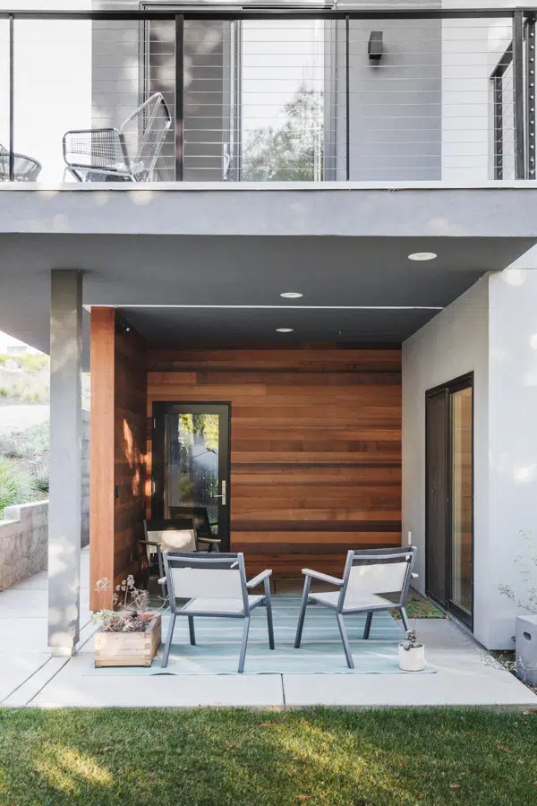 A patio from the Tech home project, featuring stained wood accent walls, glass doors and recessed lighting. The space is under a balcony that has a wire banister.