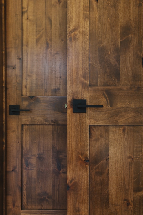 A close up on a stained wood door with black square door handles.